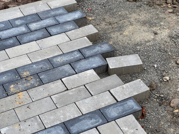 Рабочие тщательно выкладывают мощеные камни в узор, чтобы построить прочный тротуар на строительной площадке, обеспечивая точное выравнивание для долговечности.