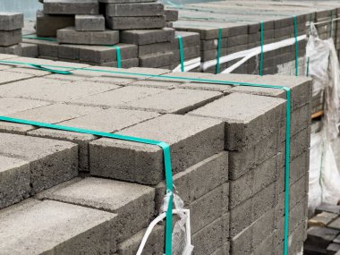 Gri tuğla kaldırımlar düzgünce istiflenmiş ve plastik ambalajlarla güvence altına alınmıştır. Şehir kaldırımında kurulum için bekliyorlar. Kurulum devam eden kentsel kalkınma faaliyetlerini gösteriyor.