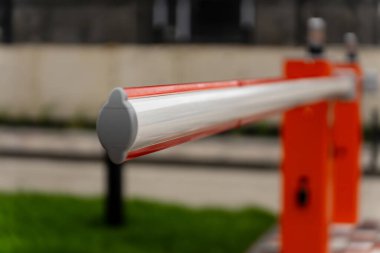 Bir bariyer kapısı kapalı duruyor, şehir ortamındaki kontrollü bir bölgeye erişimi düzenliyor. Parlak renkler güvenlik ve yönetim amacını vurguluyor.