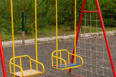 İki renkli salıncak halka açık bir parkta durur ve çocukları sallanıp oynamanın keyfini çıkarmaya davet eder. Açık hava eğlencesi ve macera için mükemmel bir ortam..