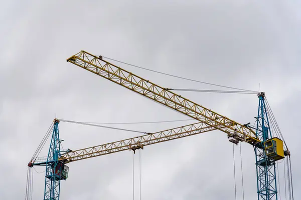 İşçiler yeni bir ev için çerçeve hazırlarken, iki büyük inşaat vinci aktif olarak bir inşaat sahasına yerleştiriliyor. Gökyüzü kapalı..