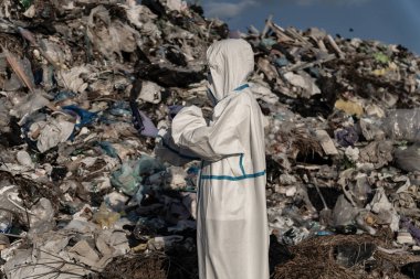 Koruyucu giysi giyen işçiler, atıklarla dolu geniş çöplüğü inceliyor ve sürdürülebilir atık yönetimi girişimlerine duyulan acil ihtiyacı vurguluyor..