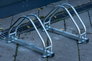 Parlak, metalik bir bisiklet parkı güneş ışığını yansıtan iyi korunmuş bir yüzeyde duruyor. Bisikletlerini rahatça ve güvenli bir şekilde korumaya çalışan bisikletçiler için mükemmel..