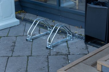 A modern bike rack is placed on a sleek pavement beside a building, surrounded by a tidy urban environment, showcasing practicality and design. clipart