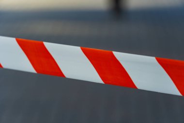 Koyu kırmızı ve beyaz çizgilerin yer aldığı canlı uyarı bandı, parlak gün ışığı altında hareketli bir şehir ortamında yasak bir bölgeye işaret ediyor..