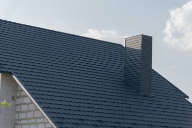 Güzel, modern bir ev, temiz çizgileri ve mimari tasarımı ön plana çıkaran şık, koyu bir çatı ile övünür. Bulutlar tembelce sürüklenirken güneş ışığı çatıdan yansıyor..