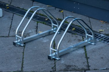 Metalden yapılmış sağlam ve modern bisiklet park yeri kaldırımda duruyor, hareketli bir şehir ortamında sürücüler için bisikletleri desteklemeye hazır..