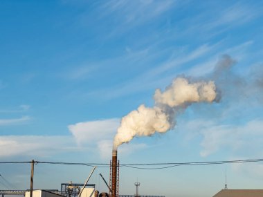 Sabahın erken saatlerinde, uzun bir endüstriyel bacadan beyaz bir duman bulutu yükselir, parlak mavi gökyüzü ile çelişir. Barışçıl atmosfer aktivitenin yeniden başladığını gösteriyor..