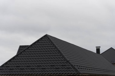 Çatılarda, bulutlu gökyüzünün altındaki bir yerleşim bölgesinde modern evler için şık ve dayanıklı bir örtü sağlayan parlak metalik fayanslar yer alıyor..