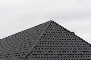 Metalik kiremitlerle kaplı şık, modern bir çatı, bir konut evinin mimarisini tamamlıyor. Ayar, çağdaş tasarımı geliştiren bulutlu bir gökyüzüne sahiptir..