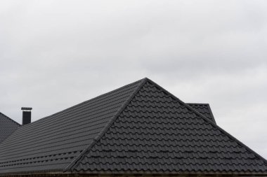 Metalik fayanslar iki modern evin çatılarını kaplıyor, bulutlu gökyüzünün ortasında parlak bir tasarım sergiliyor, çağdaş konut inşaatının altını çiziyor.