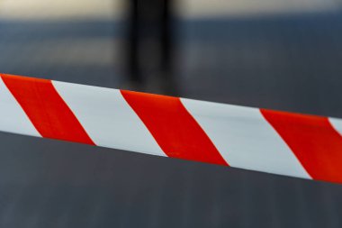 Parlak kırmızı ve beyaz uyarı bantları, kentsel bir ortamda yasak bir bölgeye işaret ediyor. Tehlike ve ihtiyat gerektiğinin işareti. İnsanlar arka planda görünür, şehir hayatını vurguluyorlar..
