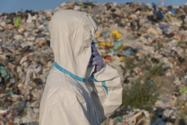 Koruyucu dişli bir işçi, çöp ve plastik atıklarla dolu büyük bir atık sahasını inceleyerek, çevre kirliliği ve atık yönetimi sorunlarına dikkat çekiyor.