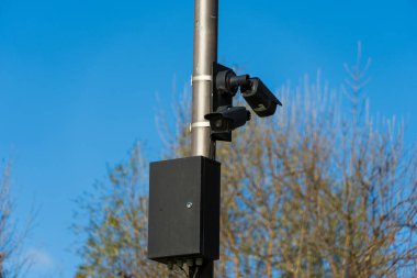 Güvenlik kameraları metal kutuplara güvenli bir şekilde yerleştirilmiş ağaçlarla çevrili bir açık alanda açık mavi gökyüzü koşulları sırasında çevreyi etkin bir şekilde izliyorlar..
