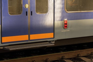 Modern elektrikli tren kapılarının şaşaalı tasarımı, batan güneşten gelen sıcak ışıkla aydınlanan bir tren istasyonunda göze çarpıyor. Trenler platformda yolcuları bekliyor..