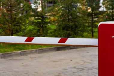 Otoparkın girişinde izinsiz girişi engelleyen bir bariyer kapısı var. Çevrede yeşil alan bulunmakta ve bu bölgede güvenlik ihtiyacını vurgulamaktadır..