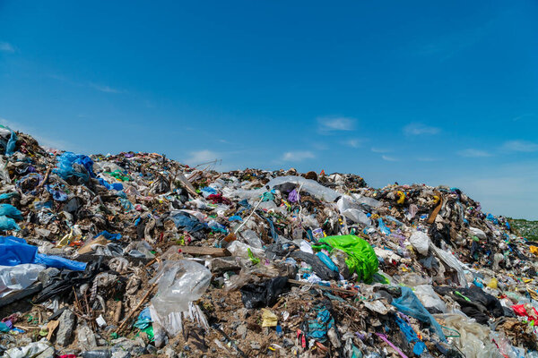 A vast landfill overflowing with trash and plastic debris contrasts starkly against a bright blue sky, highlighting the critical issue of waste management and pollution affecting ecosystems.