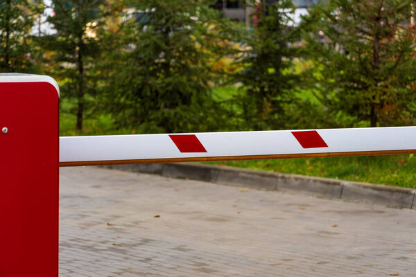 An automatic security barrier is positioned at the entrance of a parking lot, ensuring controlled access and safety for vehicles. The closed gate features red and white markings.