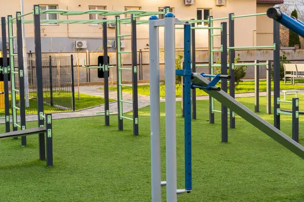 Yeşil bir parkta çeşitli egzersiz makineleri düzenlenerek fitness eğitimi için davet edici bir alan sağlanmaktadır. Bölge temiz ve sağlıklı bir yaşam tarzı için tasarlanmış..