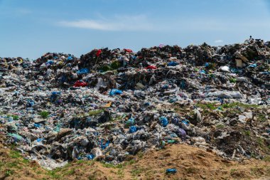 Açık mavi gökyüzünün altında, plastik atık ve enkaz yığınlarıyla dolu uçsuz bucaksız bir çöplük. Site, kirliliğin çevre ekosistem ve sağlık hizmetleri üzerindeki önemli etkisini gösteriyor..