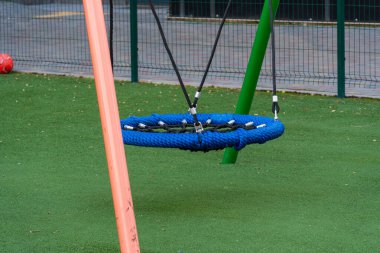 Yumuşak çimlerle çevrili canlı bir halk parkında renkli mavi bir salıncak asılı, çocukları oyun saatlerinde eğlenmeye ve eğlenmeye davet ediyor..