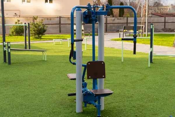 Yeşil çimenler ve diğer egzersiz alanlarıyla çevrili açık hava spor salonunda kullanıma hazır bir fitness eğitim ekipmanı, topluma sağlıklı bir yaşam seçeneği sunuyor..