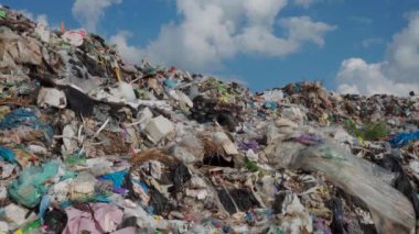 Parlak bir gökyüzü altında plastik, atık ve enkaz karışımıyla devasa bir atık alanı gösteriliyor. Atık birikimi, devam eden kirlilik sorununu ve bunun ekosistem üzerindeki etkilerini vurguluyor