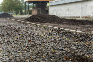 İşçiler bir şehir caddesinde ağır inşaat faaliyetlerinde bulunurken, hammadde yığınları yeni derecelendirilmiş kaldırımı kaplıyor.