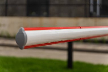 Kırmızı ve beyaz bir bariyer kapısı bir otoparkın girişinde sıkıca durur ve net bir sınır oluşturur. Geçit güvenlik ve denetimi vurguluyor, araçlar ve yayalar için güvenliği artırıyor.