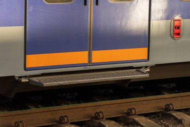 Parlak renkli elektrikli tren kapıları açık duruyor, kalabalık bir tren istasyonunda yolculara açık. Sabah güneşi platformda yumuşak gölgeler bırakıyor, yolcuları gemiye davet ediyor..