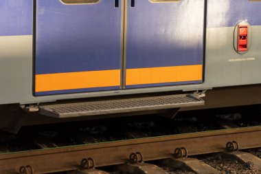 Metalik tren kapıları gezginler için hazır, alacakaranlık yaklaşırken yumuşak, altın bir ışıkla yıkanmış. Pist kenarındaki yeşillik istasyonun sakinleştirici atmosferine huzur katıyor..