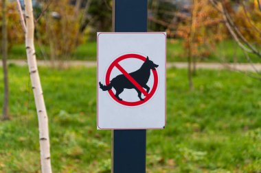 Açık hava boşluğunda açık bir uyarı işareti duruyor, kırmızı bir dairenin üzerine köpek resmi çizilmiş..