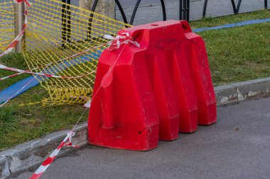 Yol kenarında belirgin bir kırmızı plastik bariyer duruyor. İşçiler yaklaşan inşaata hazırlanırken dikkat bandıyla kordon altına alındı. Güneş ışığı bölgeyi aydınlatarak görüş mesafesini arttırır..