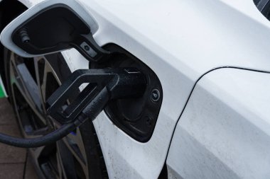 Halka açık bir istasyonda elektrikli bir araba şarj ediliyor, aracın güç bağlantısının yenilikçi tasarımı sergileniyor.
