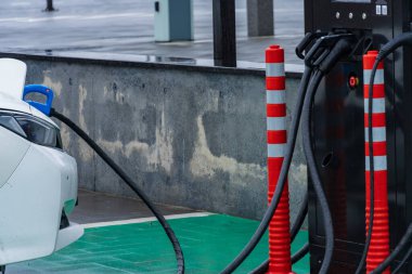 Elektrikli arabalar için tasarlanmış çağdaş bir istasyonda, arabayı istasyona bağlayan kablolarla elektrikli bir araç şarj ediliyor..