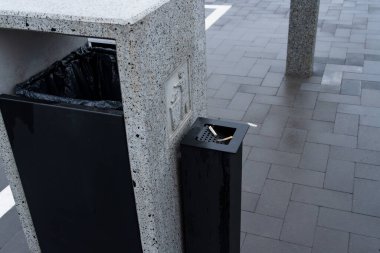 Şık ve çağdaş bir çöp konteynırı, sorumlu atık yönetimini teşvik etmek için tasarlanmış kalabalık bir kamu alanında duruyor..