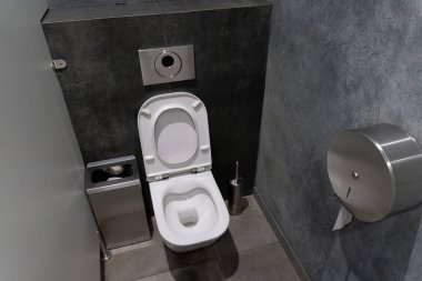 Temiz ve modern bir tuvalet desenli bir duvara dayalı beyaz bir tuvalet gösteriyor. Bitişiğinde, minimalist dekoru tamamlayan metalik bir atık kutusu, hijyen ve basitliği vurguluyor.