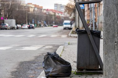 Şehir sokaklarında bir geri dönüşüm kutusunun yanına bırakılan siyah çöp torbaları, çevre koruma ve atık imhası sorunlarının altını çiziyor.