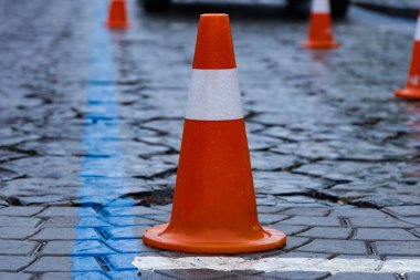 Trafik konileri, ıslak kaldırım taşları ve yağmurlu kentsel koşullar altında geçici bir inşaat alanı oluşturacak şekilde kurulmuştur..
