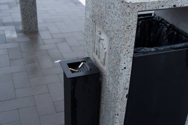 Kamu alanlarında sigara imhası için belirlenmiş bir alana sahip katı bir atık konteyneri bulunmakta olup, çevresel koruma çabaları teşvik edilmektedir.