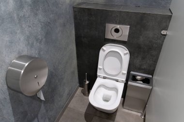 Modern bir tuvalette minimalist bir tuvalet ve verimli bir atık imha ünitesi temiz gri duvarlar ve parlak tasarım zeminine karşı sergileniyor..