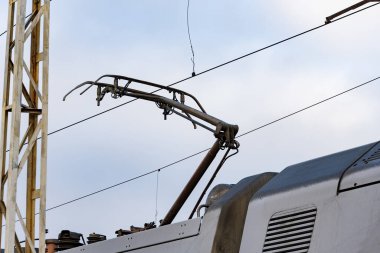 A close-up view of an electric train's pantograph raising to make contact with the overhead line for power at a railway station. clipart