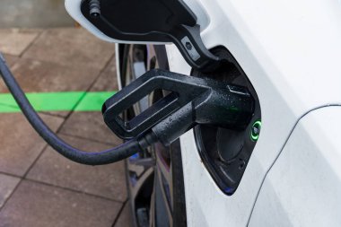 Elektrikli araç bir şarj istasyonuna bağlanıyor, yenilenebilir enerji teknolojisi ve sürdürülebilir ulaşım uygulamalarına bağlılık sergiliyor.