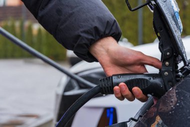Bir elektrikli aracı şarj istasyonuna bağlıyor, yağmurlu havalarda sürdürülebilir taşımacılıkta gelişmiş teknoloji sergiliyor..