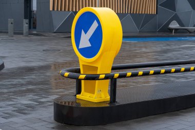 Şehir merkezindeki çağdaş bir otoparkın kaldırımında parlayan yağmur suyu gibi parlak sarı bir tabela aşağıya doğru işaret ediyor..