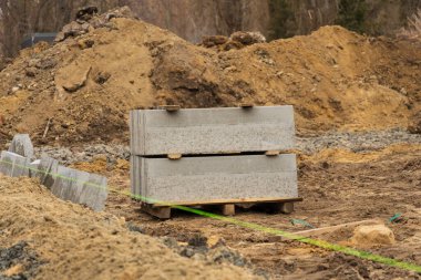 Çakıl ve beton bloklar bir inşaat sahasında dinleniyor, işlek bir şehir yolu boyunca sanayi bölgesinde devam eden onarımları vurguluyorlar..