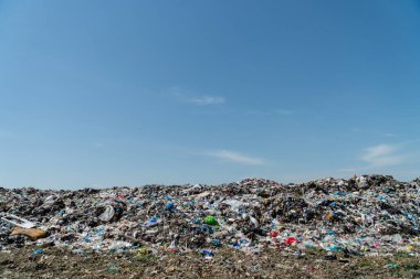 Mavi gökyüzü ile çevrili bir çöp sahasında büyük bir plastik atık birikiyor ve çevresel bir endişenin altını çiziyor..