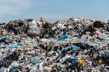 Plastik, kağıt ve diğer atık yığınları kentsel bir bölgede güneşli bir günde bir çöp sahasının arazisine hakim oluyor..