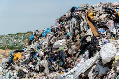 Çöp sahasındaki büyük bir çöp yığını, temiz bir gökyüzü altında devam eden atık yönetimi sorunlarını vurgulayan plastik ve enkazı gösteriyor..