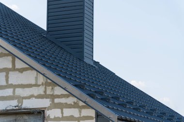 Yakın zamanda yapılmış metal bir çatının bacayı ve çevresindeki inşaat elementlerini vurgulayan detaylı bir görüntüsü..